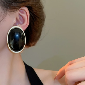 Gros plan sur boucle d'oreille ovale en résine noire avec contour en métal doré mat