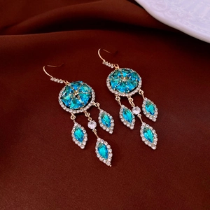 Detailed close-up of vintage gold tassel earrings with blue gemstones on silk background