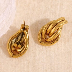Close-up of chunky gold-plated interlocking oval chain earrings on a textured stone surface