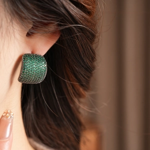 Gros plan macro sur les boucles d'oreilles incurvées en zircon vert émeraude vintage