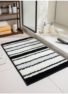 Detail of soft tufted bathroom mat with black, white, and gray stripes on white tile floor