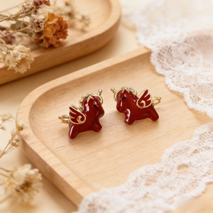 Detailed close-up of red oil-drop Pegasus stud earrings on a vintage wooden tray