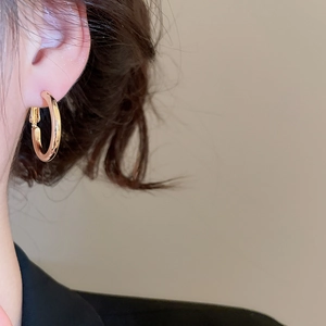 Close-up of minimalist gold hoop earring worn by a model against a warm grey wall