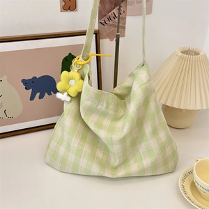 Close-up of green checkered canvas tote bag with a yellow flower pendant on a desk