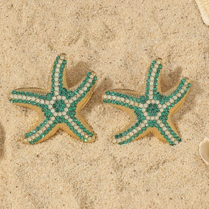 Detailed close-up of starfish earrings with green and white crystals on sand
