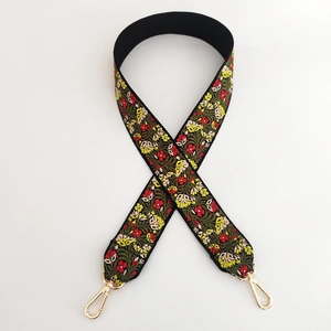 Detail of floral embroidery on wide black bag strap with gold metal lobster clasps