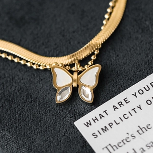Detail of a double-layered gold butterfly necklace with white shell inlay and crystals