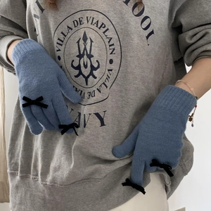 Detailed close-up of blue knitted gloves with black bow accents worn by a model