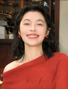 Close-up of red flower stud earrings worn with a red knit top in a cozy warm cafe setting