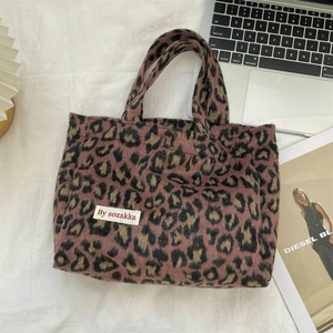 Detail of leopard print plush tote bag with fabric logo tag on soft textured background