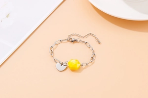 Detail of silver chain bracelet with yellow hexagonal gemstone and heart charm