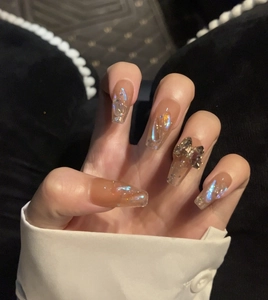 Detail of luxury press-on nails with nude tint, glitter, and a metal butterfly charm