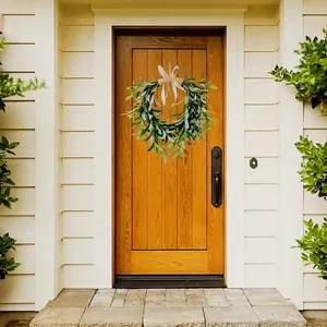 Artificial green olive leaf wreath with a beige bow hanging on a classic white wooden door