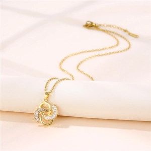 Elegant gold knot pendant necklace with inlaid zircon crystals on a soft white fabric background