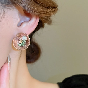 Close-up of floral enamel earring with white pearl detail worn on model's ear