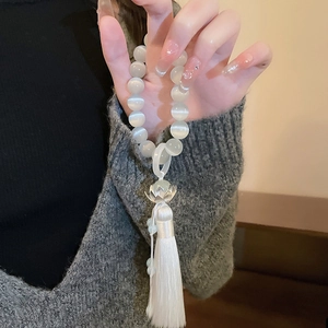 Detailed shot of cat eye bead bracelet with silver lotus charm and white silk tassel