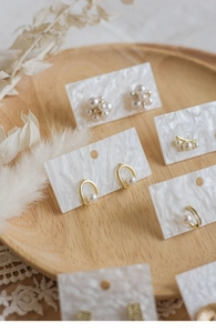 Close-up of elegant pearl earrings on white cards with lace and floral background
