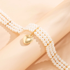 Macro detail of triple-layer pearl necklace with a polished gold heart pendant