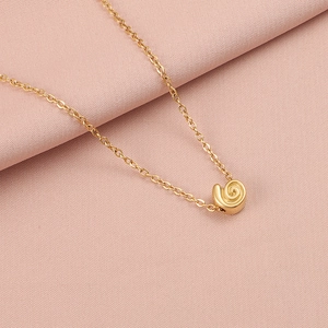 Close-up of golden spiral shell pendant on a fine chain over pink fabric background