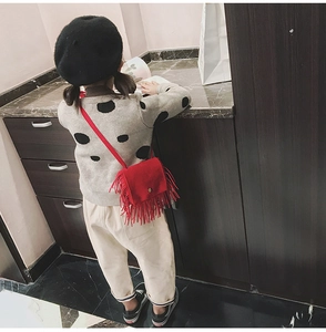 Detail of red tassel crossbody bag for kids featuring suede texture and metal buckles