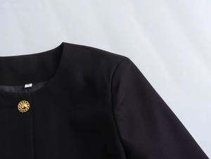 Detail of black textured round neck jacket with retro golden button and size tag
