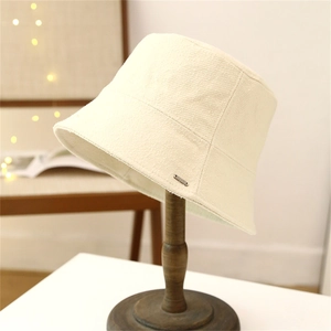 Cream textured bucket hat with raw edges on a vintage stand against a soft warm background