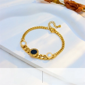 Macro detail of golden Cuban chain bracelet with Roman numeral and shell pendants