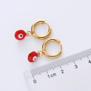 Détail de boucles d'oreilles créoles dorées avec pampilles œil grec rouge et échelle