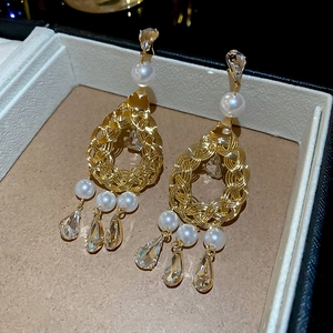 Close-up of golden woven earrings with white pearls and crystal water drop pendants