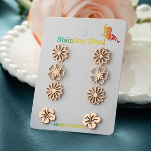 Close-up of four pairs of rose gold stainless steel floral earrings on a display card
