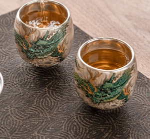 Macro shot of silver-plated dragon teacup with tea being poured into the double-wall cup