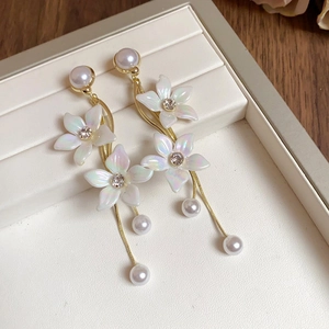 Détail de boucles d'oreilles fleuries avec chaînes dorées, perles et pétales irisées