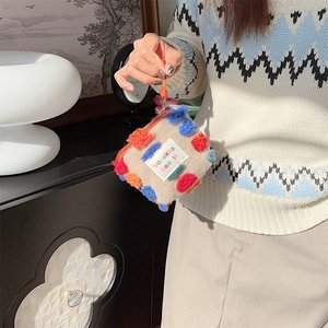 Detail of plush beige bucket bag with colorful pom-poms and sozakka beaute label