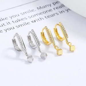 Detailed macro view of D-shaped silver and gold hoop earrings with small cubic pendants