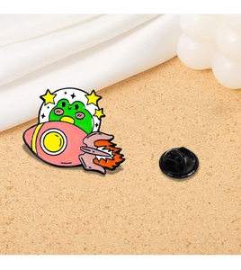 Detail of a cartoon frog riding a rocket enamel pin with a black rubber clutch backing