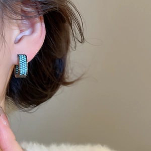 Close-up of black huggie earrings with turquoise pavé stones worn by a model