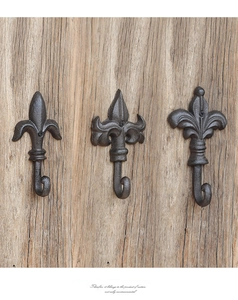 Detailed close-up of three vintage cast iron wall hooks with fleur-de-lis design on wood