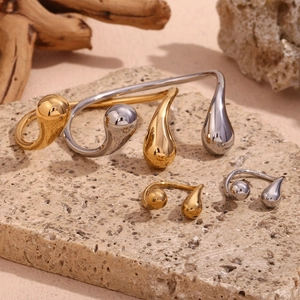 Polished gold and silver teardrop rings displayed on natural stone and wood