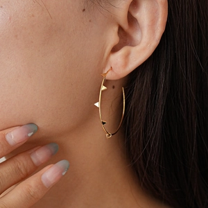 Detailed close-up of a large gold geometric earring with triangular accents on a model