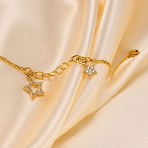Macro detail of 18K gold star bracelets with zircon pavé setting on satin fabric