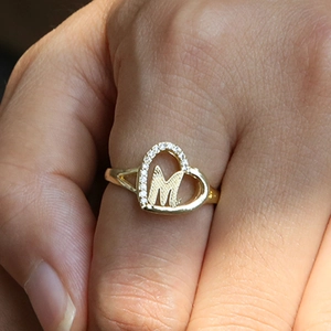 Gold heart-shaped ring with pavé stones featuring a cursive letter M on a hand