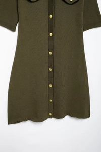 Detail of dark green knit dress featuring golden buttons and scalloped edge hemline