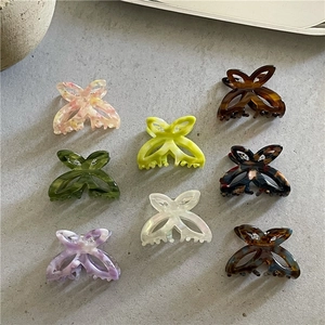 Flat lay of eight colorful acetate butterfly hair claws on a textured grey surface