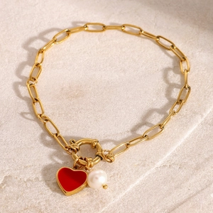Macro detail of 18k gold plated bracelet with red enamel heart and white pearl charm