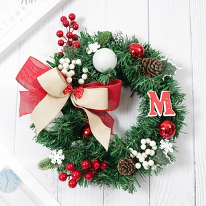 Christmas wreath with red berries, pine cones and a red letter M on white wood background