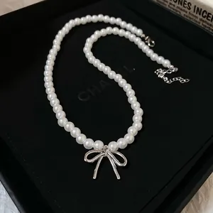 Gros plan d'un collier ras du cou en perles avec pendentif noeud métallique