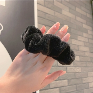 Close-up of a soft black plush scrunchie showing the fluffy texture and elastic band