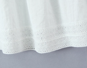 Detaillierte Nahaufnahme der aufwendigen Lochstickerei auf einem weißen Sommerkleid