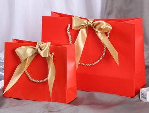 Detail of red gift bags with gold bow ribbons and matching woven handles on a white fabric