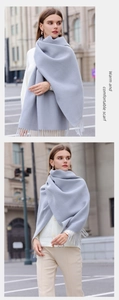 Detail shot of a grey soft cashmere-like scarf with tassels worn by a model in a city